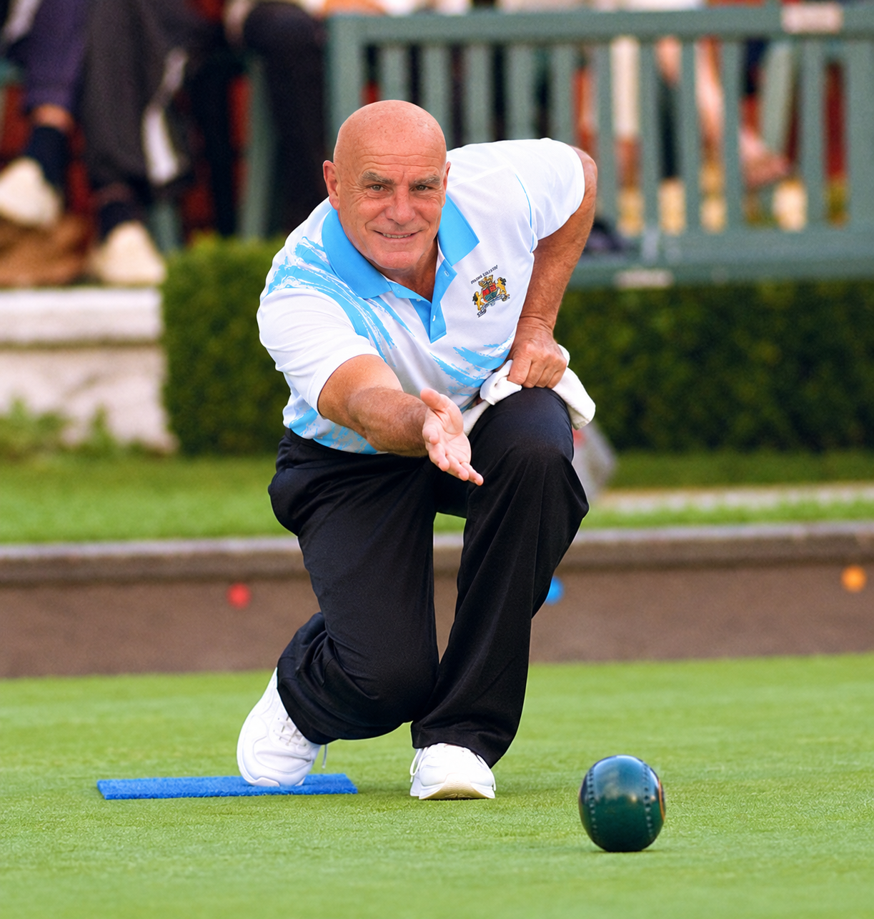 Lawn bowler wearing the City of Cambridge Bowls Club shirt delivering a bowl on the green